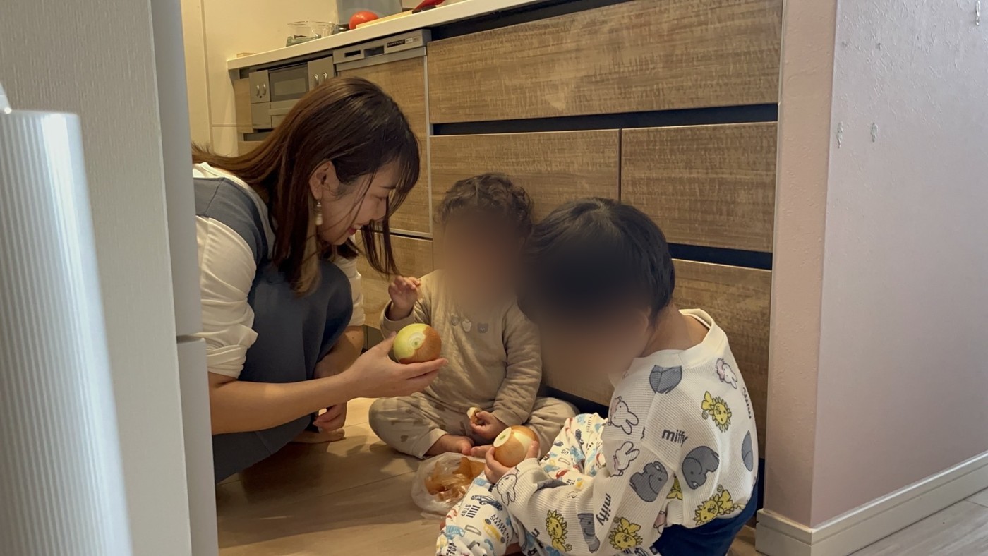 台所の床で、玉ねぎをむく2人の子どもと、声をかけるなかのかほ(お子さんの顔はぼかしています)