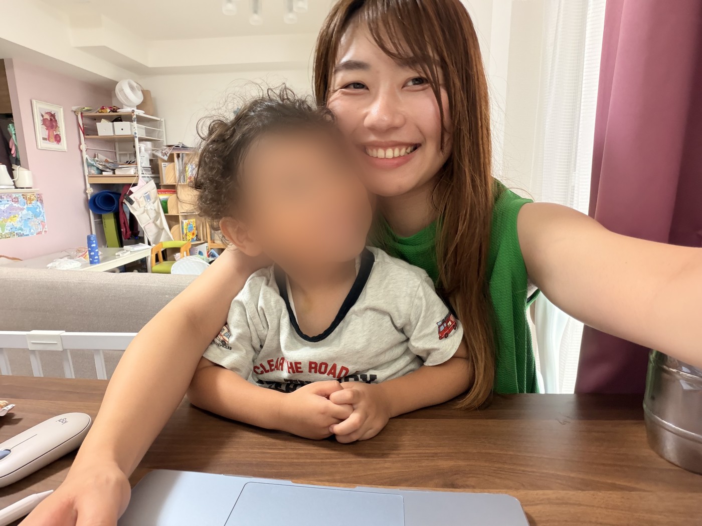 子どもを抱っこして、パソコンの前で笑うなかのかほ(お子さんの顔はぼかしています)